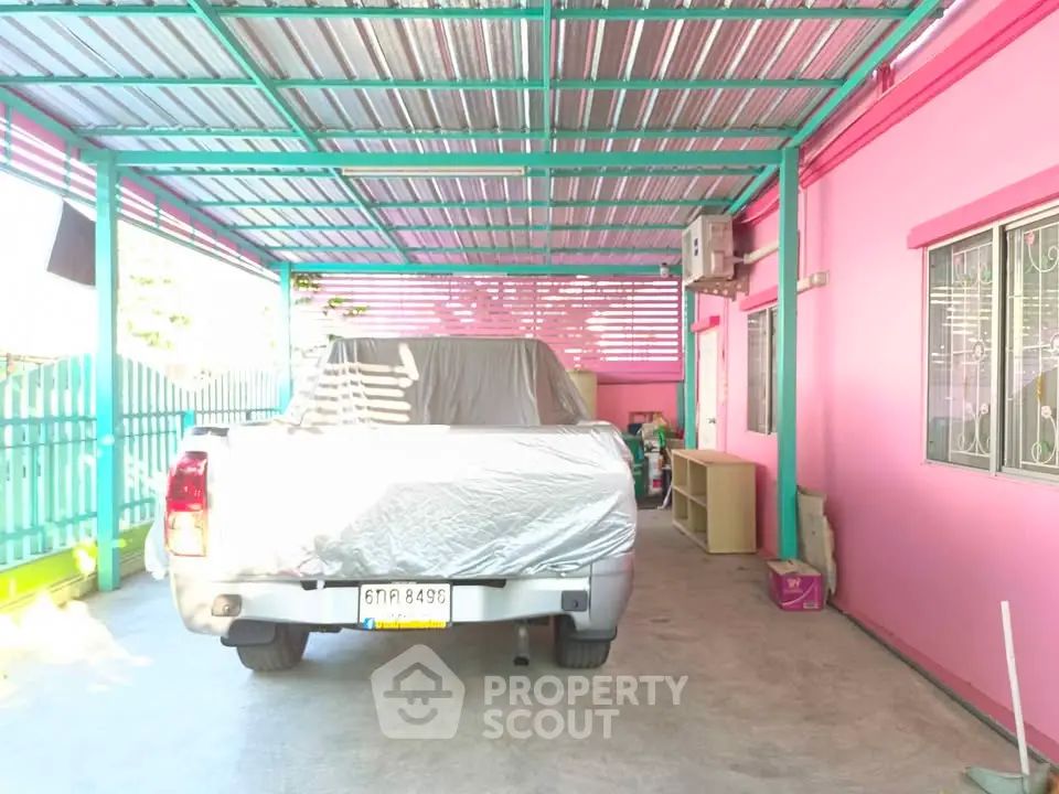 Covered parking area with vibrant pink walls and metal roof, featuring a parked vehicle.