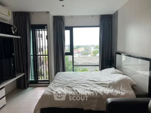 Modern bedroom with large window and balcony view in urban apartment.