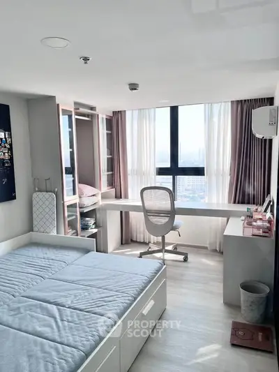 Modern bedroom with large window, study desk, and ample storage in a high-rise apartment.