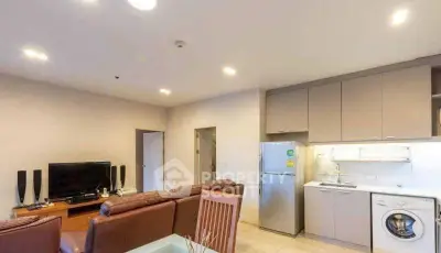 Modern living room with open kitchen, featuring leather sofas, TV, fridge, and washing machine.