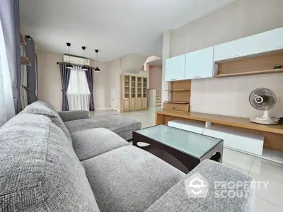 Spacious living room with modern grey sofa, sleek white storage units, and ample natural light, perfect for family relaxation and entertaining guests.