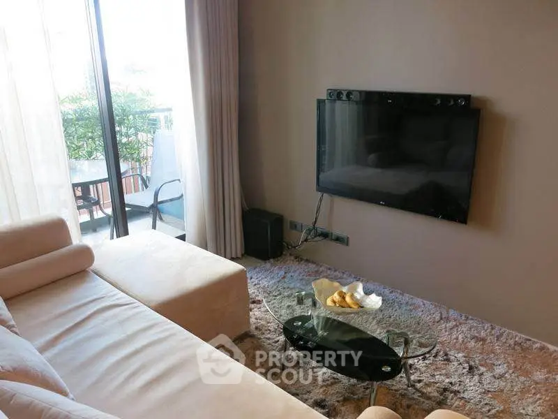 Modern living room with cozy seating and wall-mounted TV, overlooking a balcony with greenery.