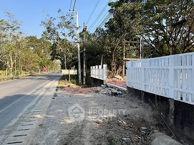 Scenic roadside view with white fence and lush greenery, ideal for real estate development.