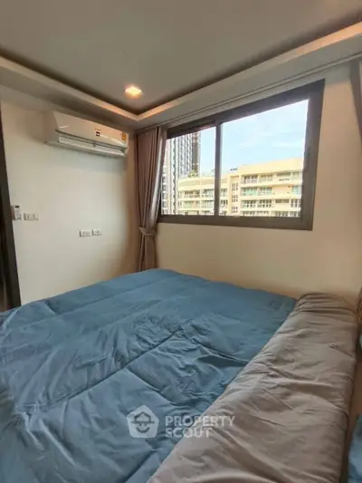 Cozy bedroom with large window offering city view and modern air conditioning unit.