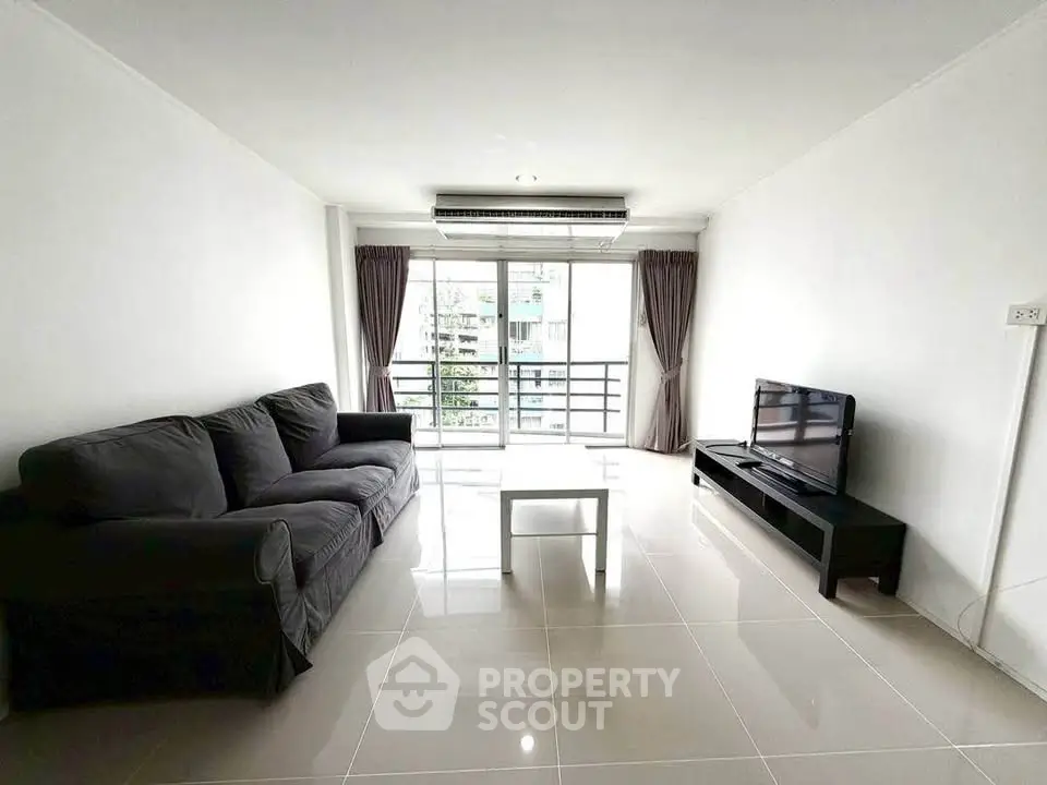 Spacious living room with modern sofa and large window offering natural light and balcony access.