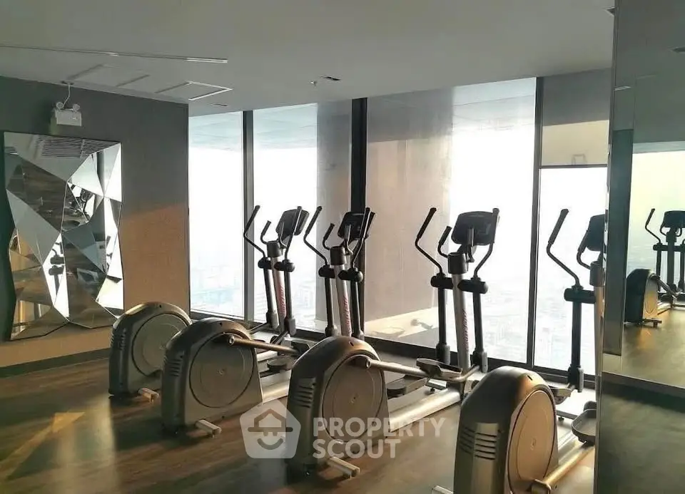 Modern gym with elliptical machines and city view in luxury high-rise building.