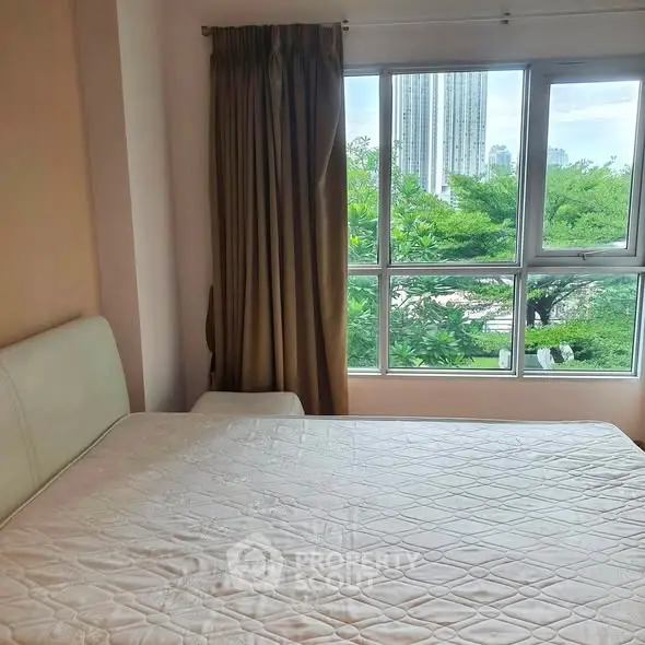Cozy bedroom with large window offering lush green views in urban setting.