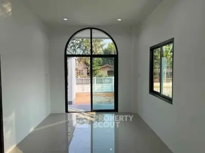 Bright room with arched window and glossy floor tiles, overlooking a serene outdoor view.