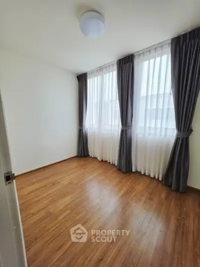 Spacious bedroom with large windows and elegant curtains, featuring sleek wooden flooring.