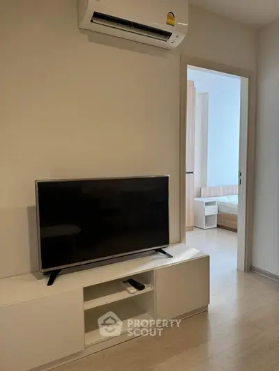 Modern living room with sleek TV unit and air conditioning, leading to a cozy bedroom.