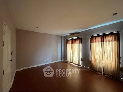 Spacious empty room with wooden flooring and large windows with curtains, perfect for customization.