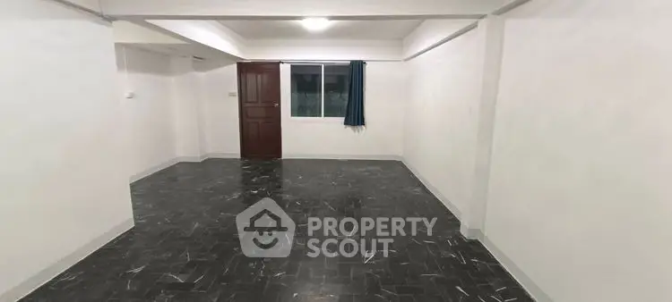 Spacious empty room with dark tiled flooring and a window, ideal for customization.
