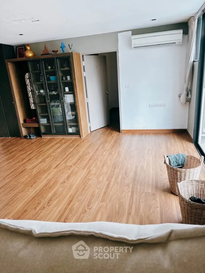 Spacious living room with wooden flooring and glass cabinet, perfect for modern living.