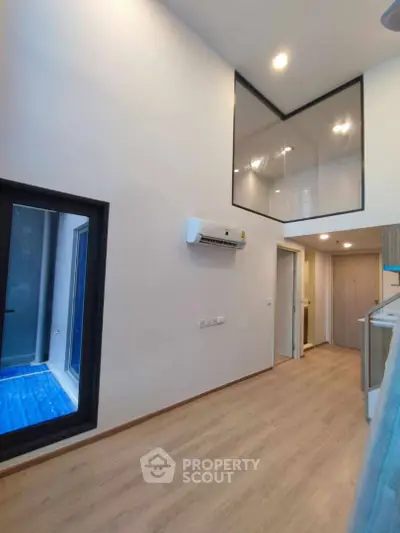 Modern interior with high ceilings and large windows, featuring a sleek air conditioning unit and wood flooring.