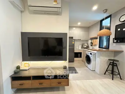 Modern living room with wall-mounted TV and adjacent kitchen featuring washing machine.