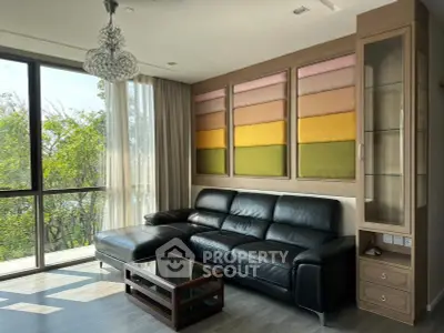 Stylish living room with black leather sofa, large windows, and colorful wall art in modern apartment.