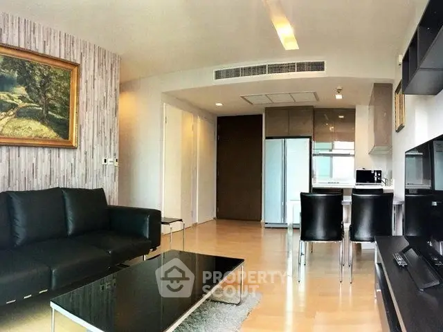 Modern living room with sleek black furniture and open kitchen layout in stylish apartment.