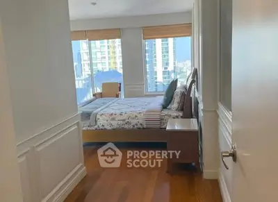Spacious bedroom with wooden flooring and large windows offering city views.