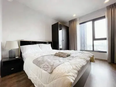 Spacious bedroom with large window and modern furnishings in a stylish apartment.