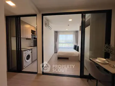 Modern studio apartment with glass partitions, featuring a cozy bedroom and compact kitchen with washing machine.