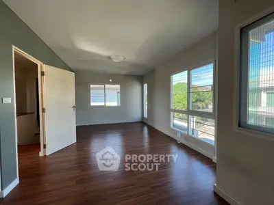 Spacious empty room with wooden flooring and large windows offering natural light.