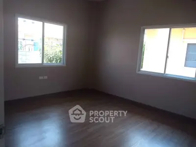 Spacious empty room with wooden flooring and large windows offering natural light.