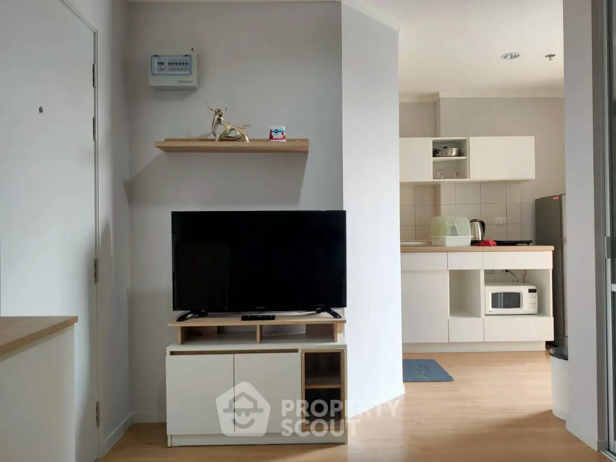 Modern apartment interior with TV and kitchen area, featuring sleek cabinetry and light wood flooring.