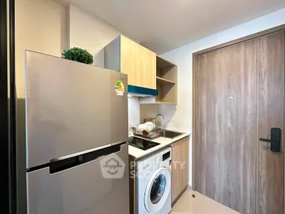 Modern compact kitchen with fridge, washing machine, and sleek cabinetry in a stylish apartment.