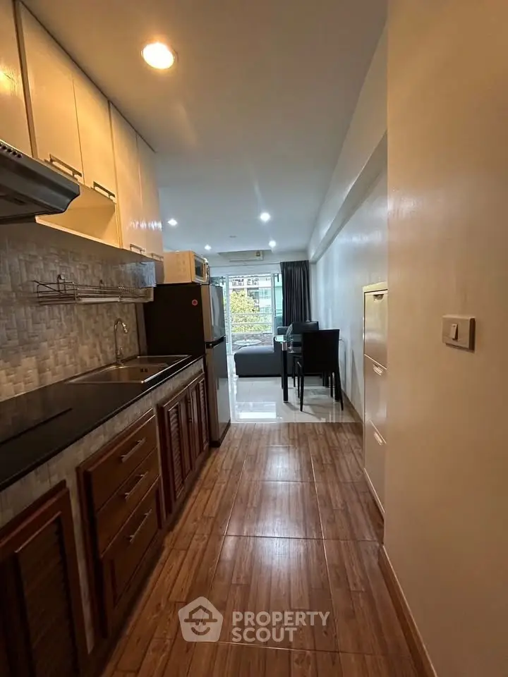 Modern kitchen with open layout leading to a cozy living area, featuring sleek cabinetry and wood flooring.