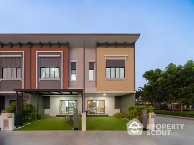 Elegant two-story townhouse with a modern facade, featuring a covered parking space and a well-manicured front lawn, captured at dusk.