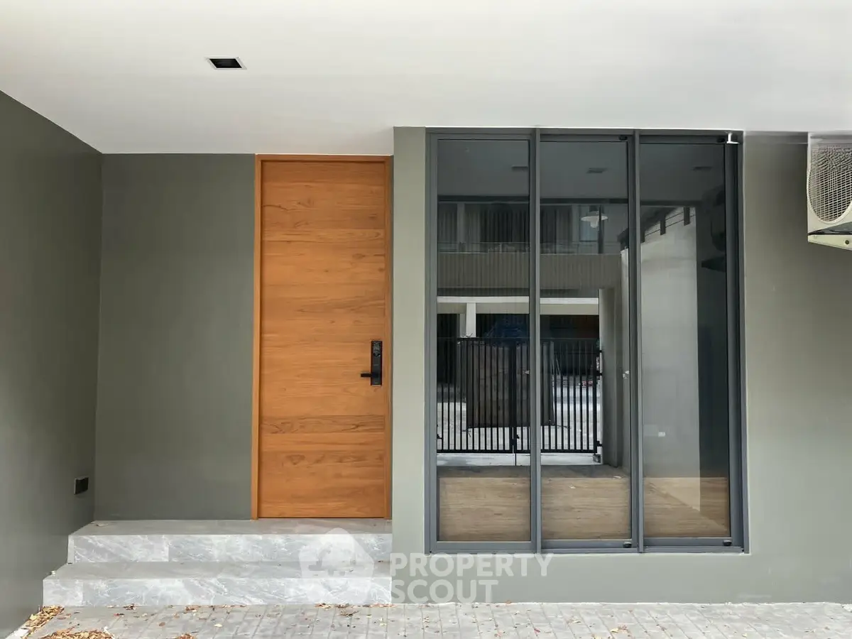 Modern entrance with sleek wooden door and large glass panels in contemporary home exterior.
