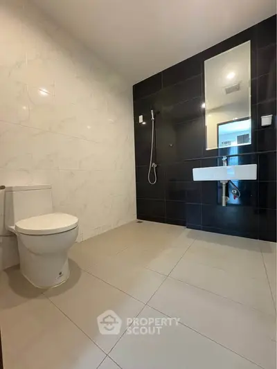 Modern bathroom with sleek black and white tiles, featuring a wall-mounted sink and toilet.