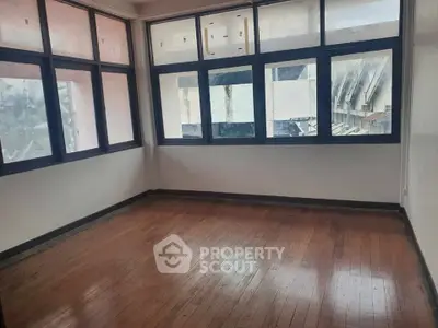 Spacious empty room with large windows and wooden flooring, ideal for customization.