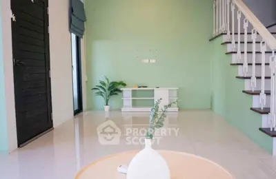 Modern living room with green walls and staircase, featuring minimalistic decor and natural light.