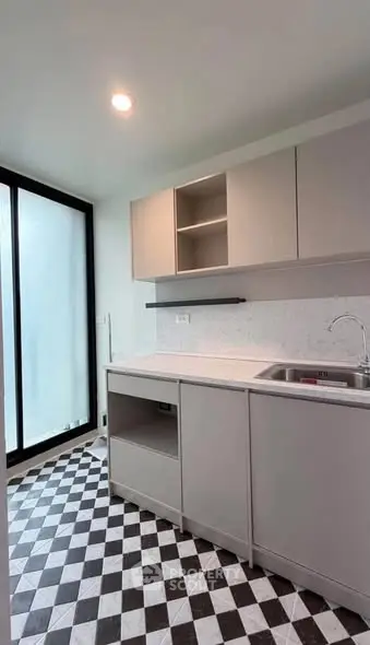 Modern kitchen with sleek cabinetry and checkered flooring, featuring a large window for natural light.