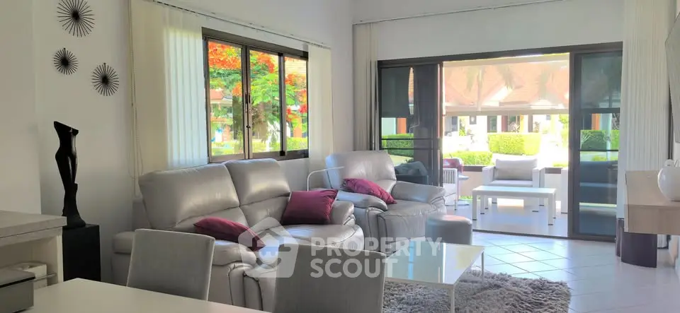 Spacious living room with modern decor and garden view, featuring plush sofas and large windows.