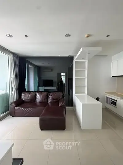 Modern living room with sleek design and open kitchen layout, featuring a leather sofa and large windows.