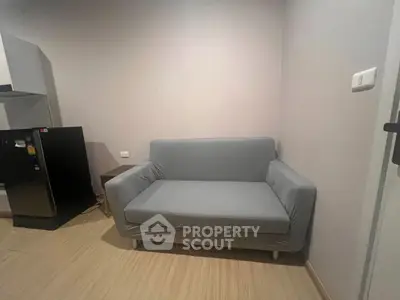 Cozy living room with modern gray sofa and compact fridge, perfect for small spaces.