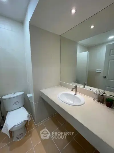 Modern bathroom with sleek design and large mirror, featuring a white sink and toilet.