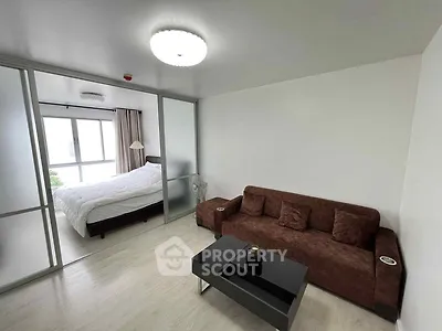 Modern living room with brown sofa and glass partition leading to a bright bedroom.