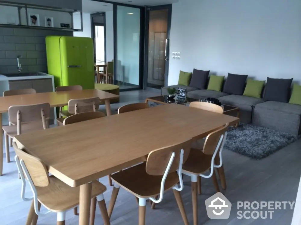 Modern open-plan living room with vibrant green fridge and stylish wooden dining set.