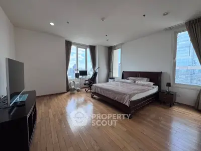 Spacious bedroom with city view, hardwood floors, and modern furnishings in a high-rise apartment.