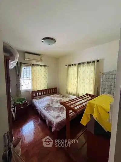 Cozy bedroom with wooden flooring and ample natural light from two windows.