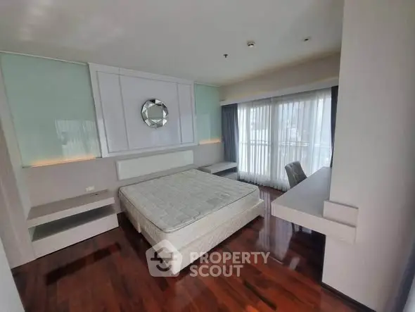 Spacious bedroom with large windows and hardwood floors in modern apartment.