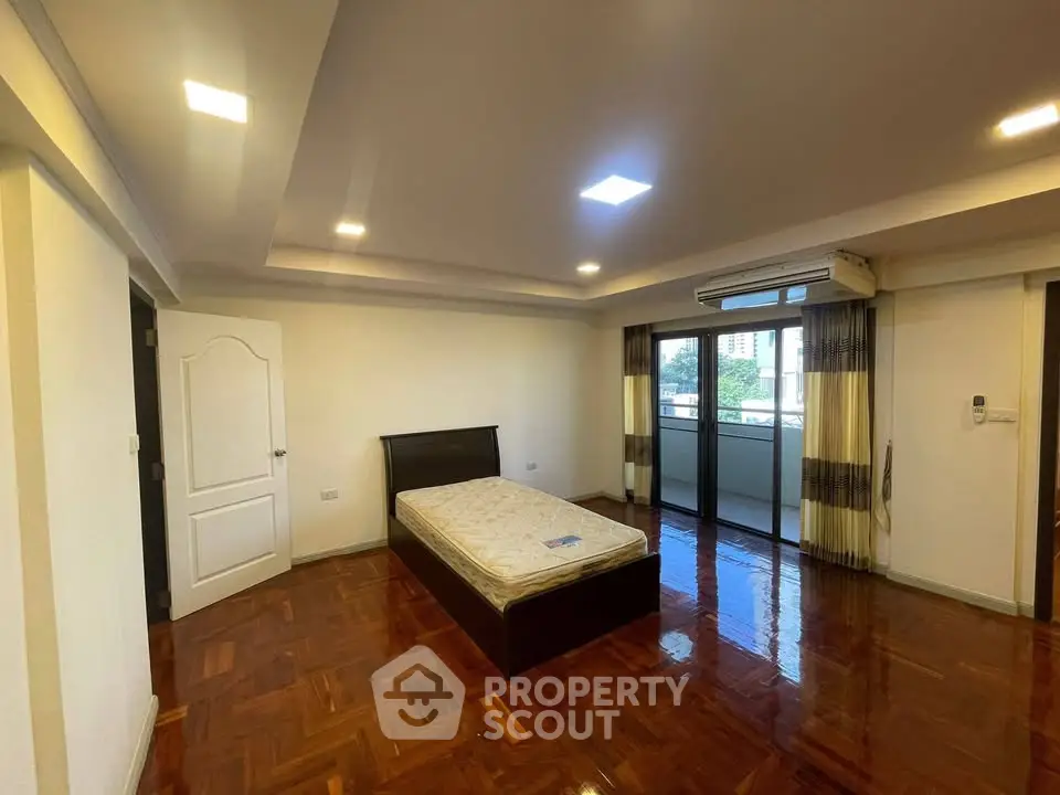Spacious bedroom with polished wooden floors and balcony access in modern apartment.