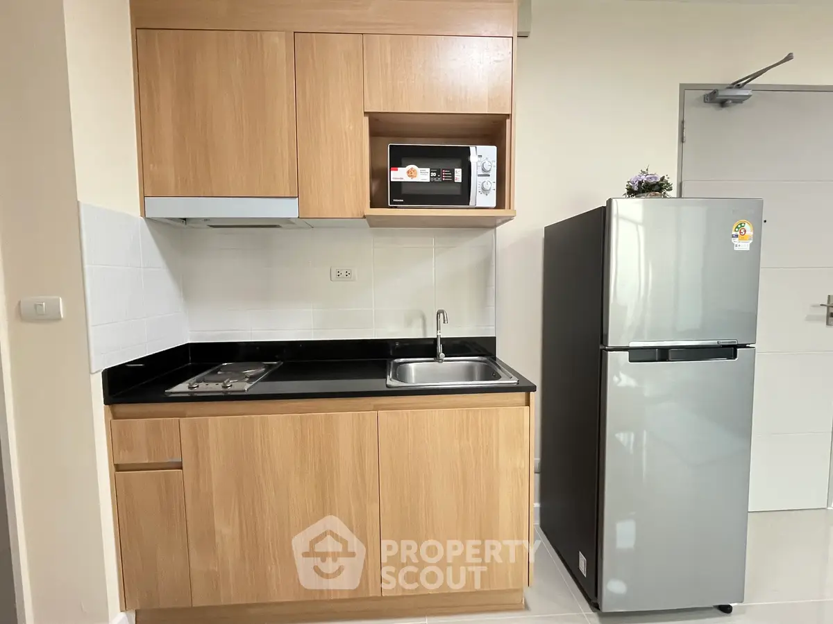 Modern compact kitchen with wooden cabinets, microwave, and stainless steel fridge.