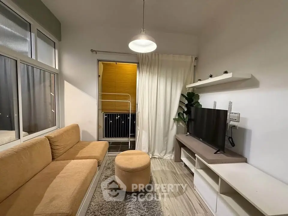 Cozy living room with modern decor and balcony access, featuring a comfortable sofa and sleek TV setup.