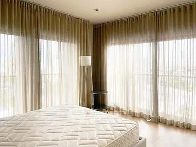 Spacious bedroom with large windows and sheer curtains, offering abundant natural light and a serene atmosphere.