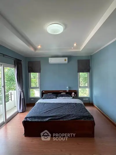 Spacious bedroom with large windows and balcony access, featuring modern decor and natural light.