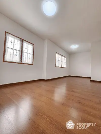 Spacious and well-lit empty room with polished hardwood floors and multiple windows offering ample natural light, ideal for a customizable living space.